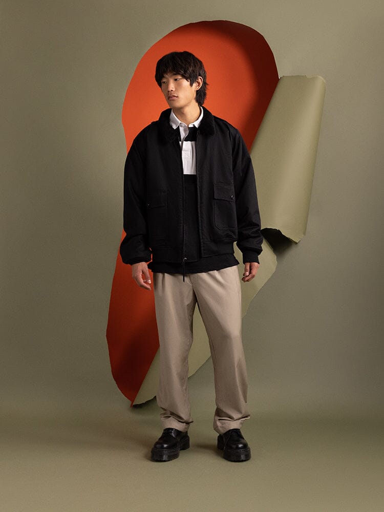 Dressed in a 1940s B-10 Bomber Jacket in black by Alpha Industries and beige pants, a person exudes confidence.
