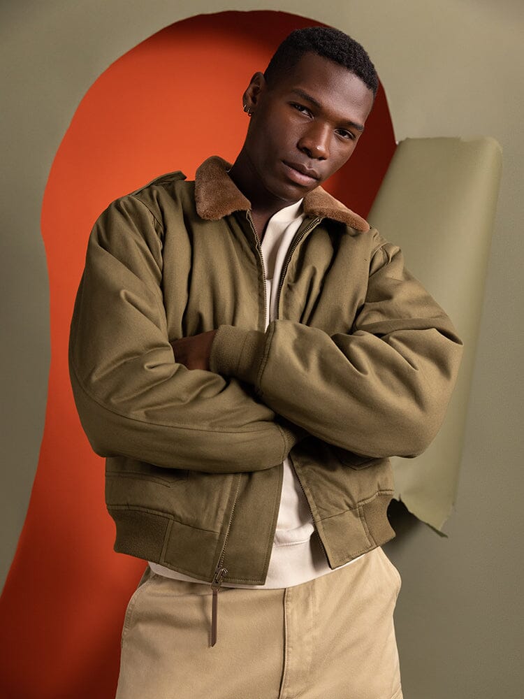 A person wearing the 1940s B-10 Bomber Jacket in olive by Alpha Industries stands with arms crossed.