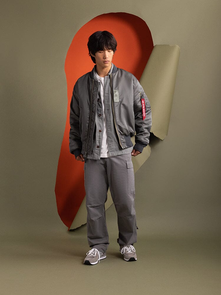 A person wearing an Alpha Industries 1960s MA-1 Bomber Jacket in field gray and matching pants.