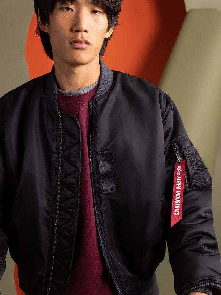 A person wearing a alack 1960s MA-1 Bomber Jacket by Alpha Industries, featuring a distinctive red tag.