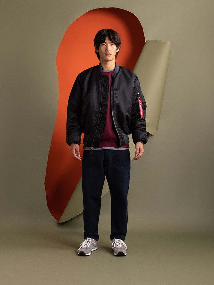 A person stands wearing an Alpha Industries 1960s MA-1 Bomber Jacket in black.