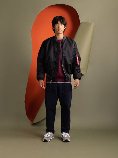A person stands wearing an Alpha Industries 1960s MA-1 Bomber Jacket in black.