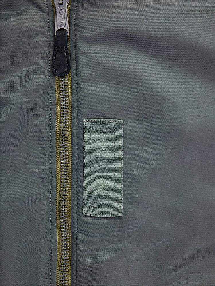 Close-up of the Alpha Industries 1960s MA-1 Bomber Jacket in field gray, showcasing a green fabric loop and detailed stitching.