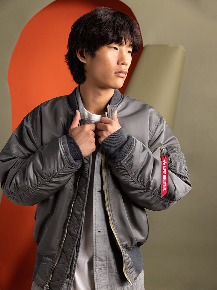 A person wearing a gray 1960s MA-1 Bomber Jacket from Alpha Industries stands, embodying a modern military look.