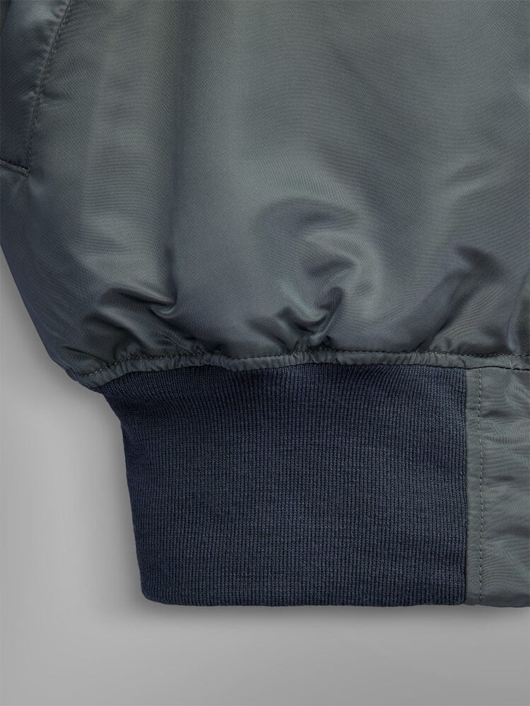 Close-up of the 1960s MA-1 Bomber Jacket by Alpha Industries in field gray, showcasing dark ribbed cuffs at the hem.