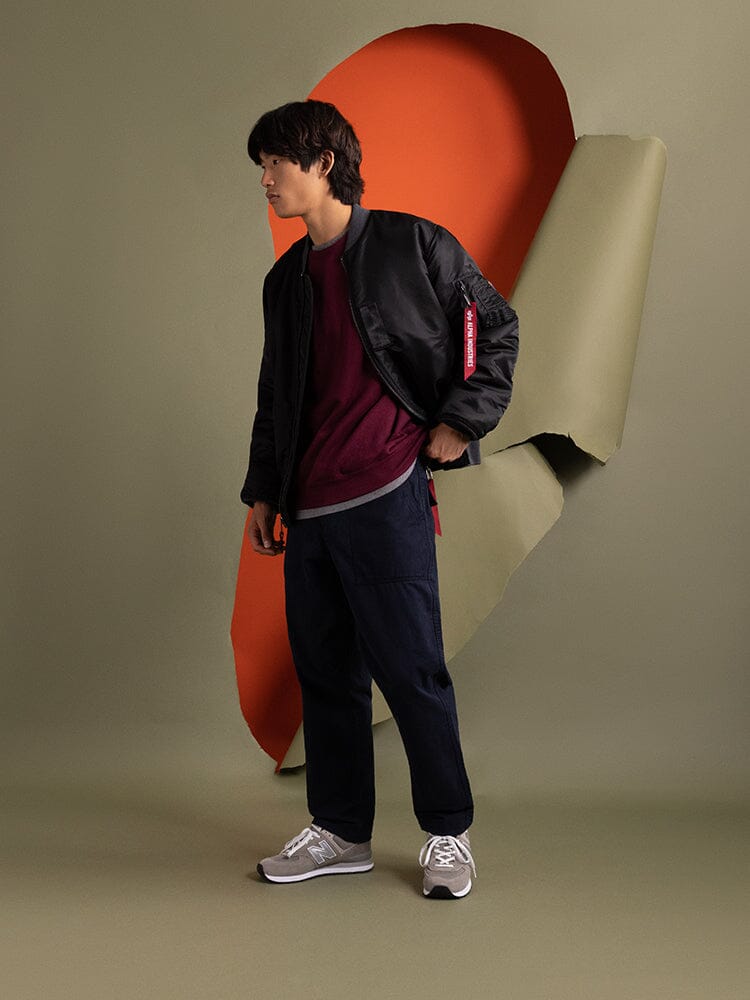Side-view of a person wearing the 1960s MA-1 Bomber Jacket by Alpha Industries over a maroon shirt.