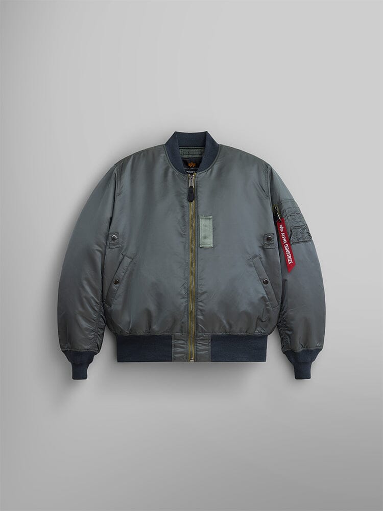 The 1960s MA-1 Bomber Jacket by Alpha Industries in Field Gray. This jacket includes a zipper closure and ribbed cuffs and hem, highlighted by a red tag on the left sleeve pocket . 