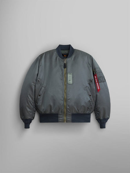 The 1960s MA-1 Bomber Jacket by Alpha Industries in Field Gray. This jacket includes a zipper closure and ribbed cuffs and hem, highlighted by a red tag on the left sleeve pocket . 