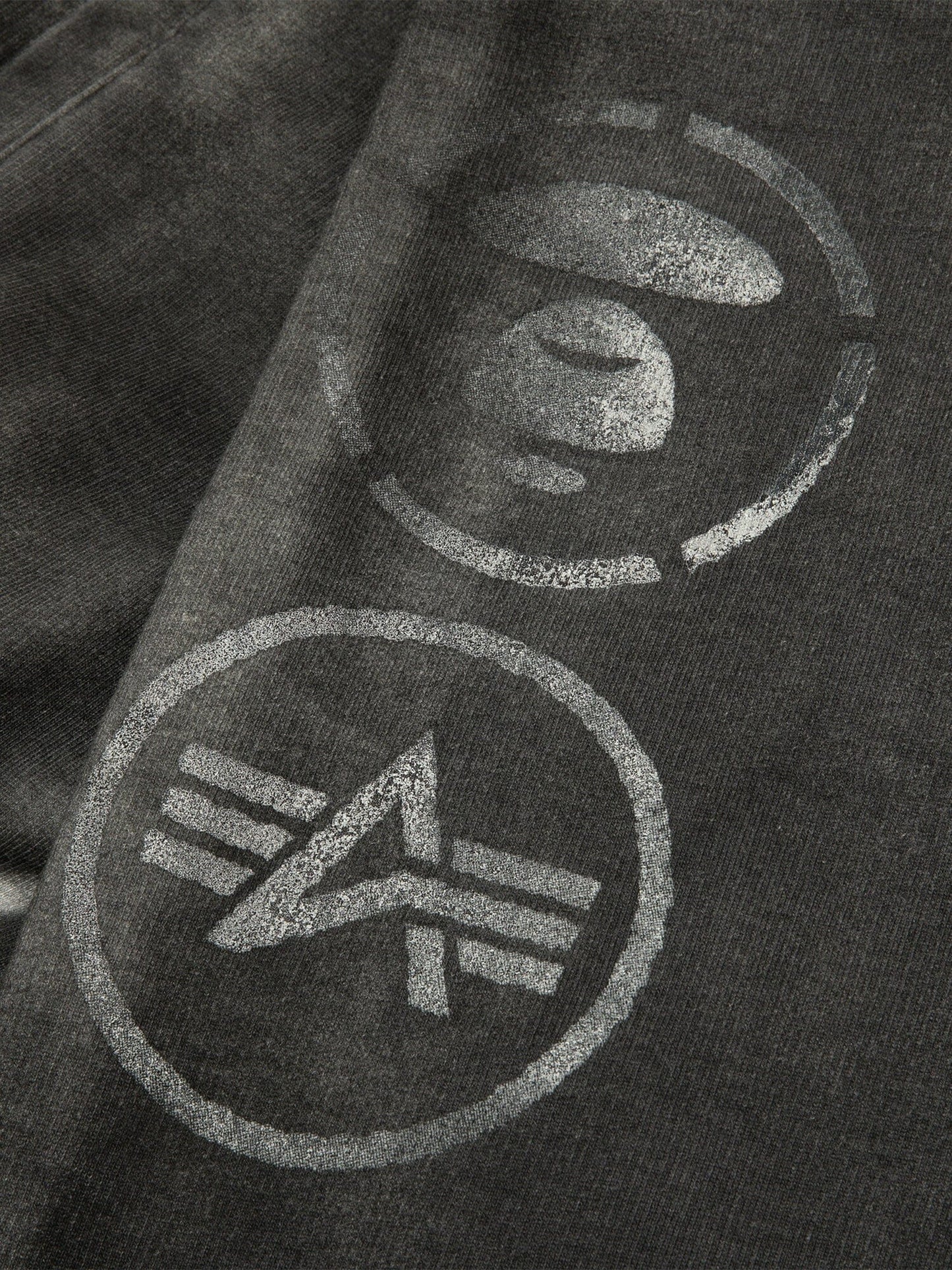 Aape X Alpha Army Sweatpant by Alpha Industries, black with two white circular logos—one with a stylized Earth, the other with geometric lines and an angled shape.