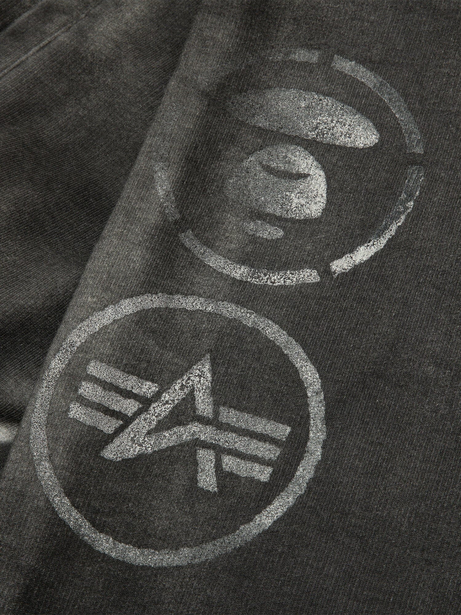 Aape X Alpha Army Sweatpant by Alpha Industries, black with two white circular logos—one with a stylized Earth, the other with geometric lines and an angled shape.