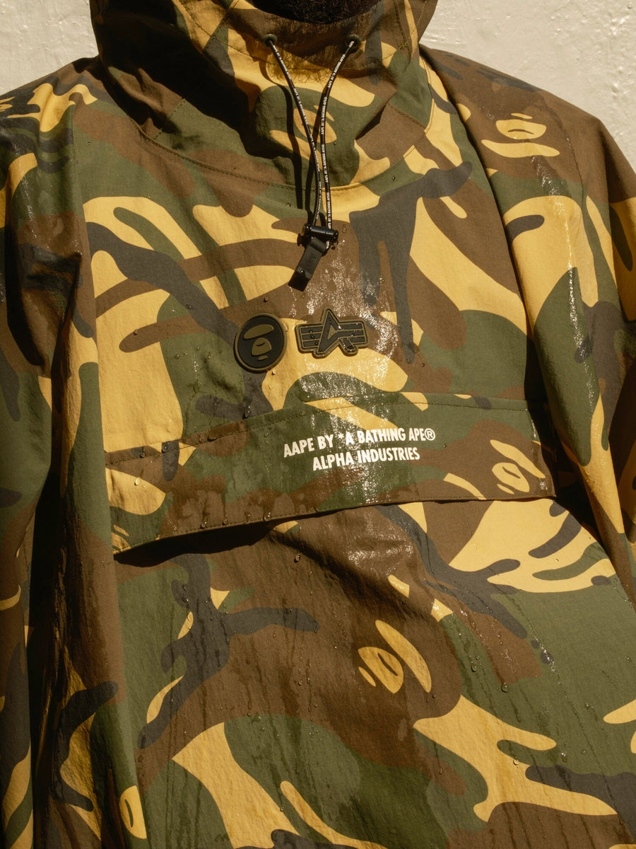 Front view of the AAPE x Alpha Industries 2 Layer Rain Jacket, Camo Print, Front Pocket with Branding, Waterproof Materials, Hood, Toggle Closure.