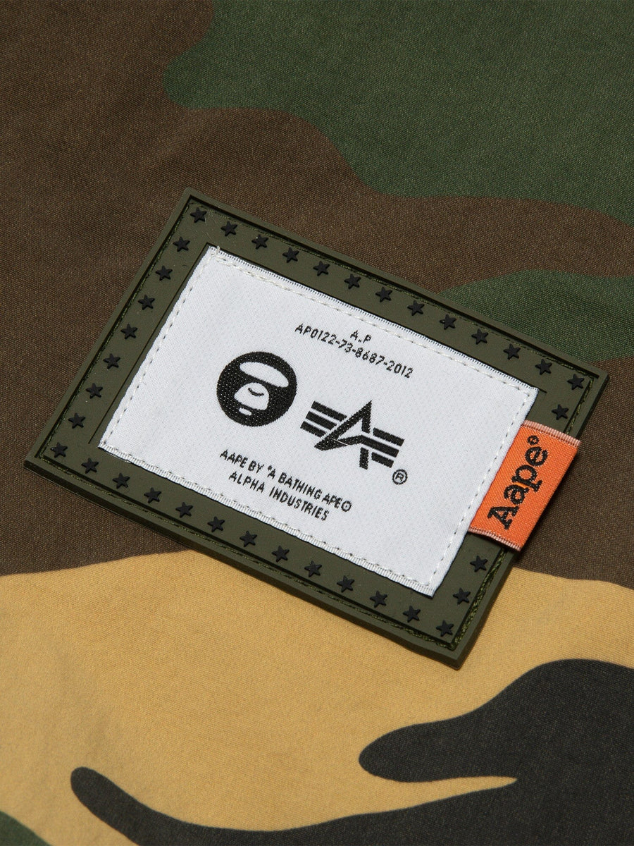 Close-up Camouflage Print Fabric with Rectangular White Label Featuring AAPE and Alpha Industries Logos, Bordered by Stars.