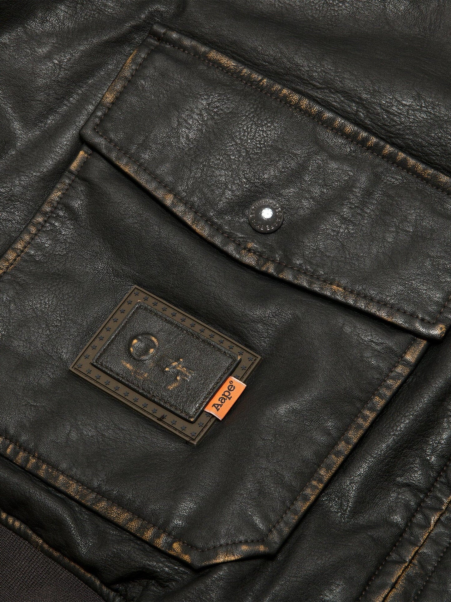 Aape X Alpha Pu Leather Quilted Jacket by Alpha Industries, black pocket with visible stitching, metal snap button, and Aape patch.