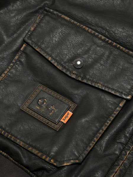 Aape X Alpha Pu Leather Quilted Jacket by Alpha Industries, black pocket with visible stitching, metal snap button, and Aape patch.