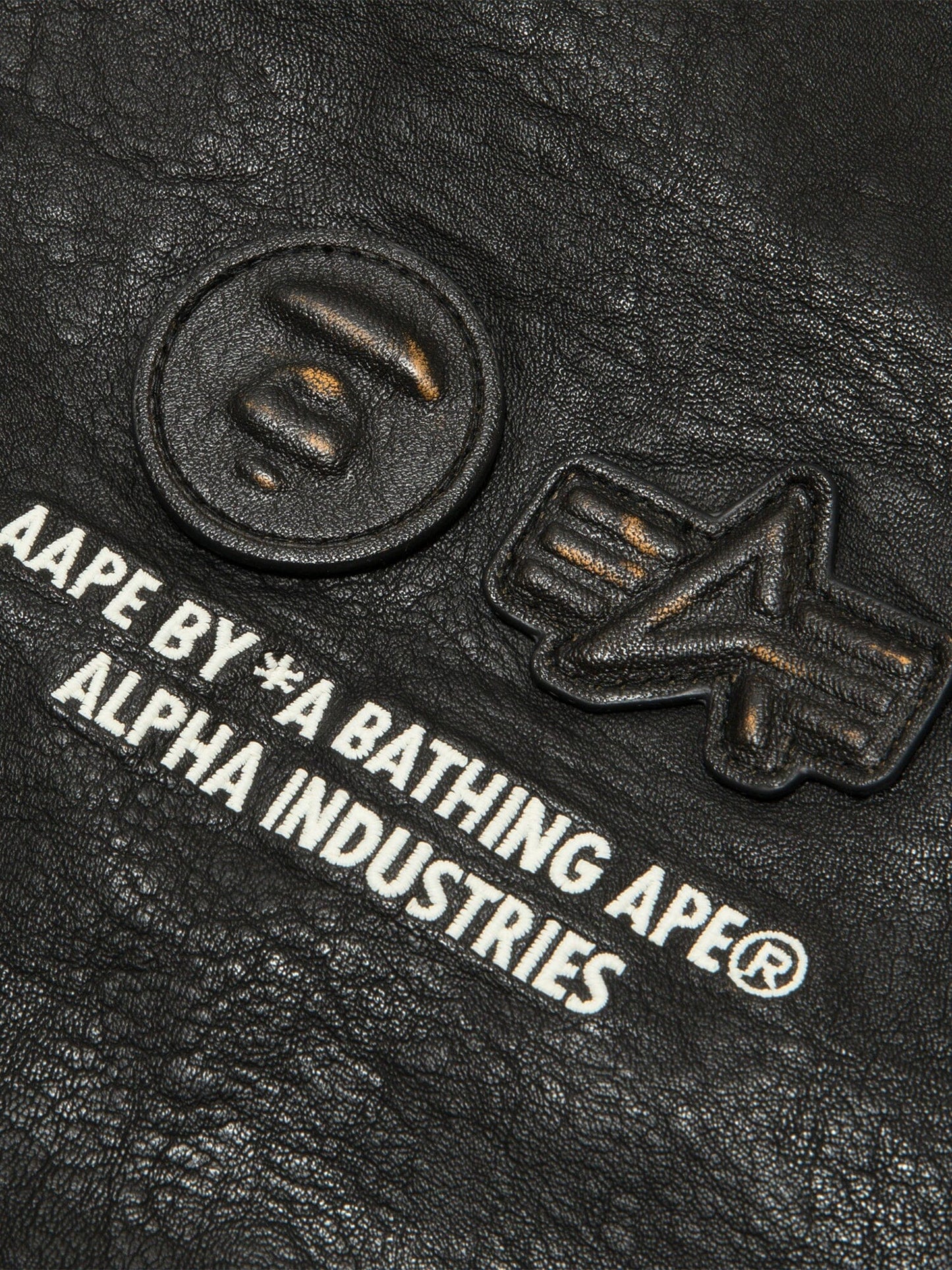 Aape X Alpha Pu Leather Quilted Jacket by Alpha Industries, black textured material with embossed logos and printed text, MA-1 design.