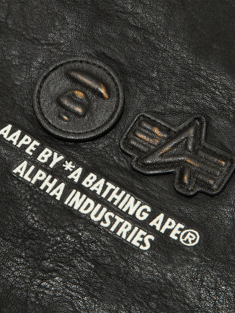 Aape X Alpha Pu Leather Quilted Jacket by Alpha Industries, black textured material with embossed logos and printed text, MA-1 design.