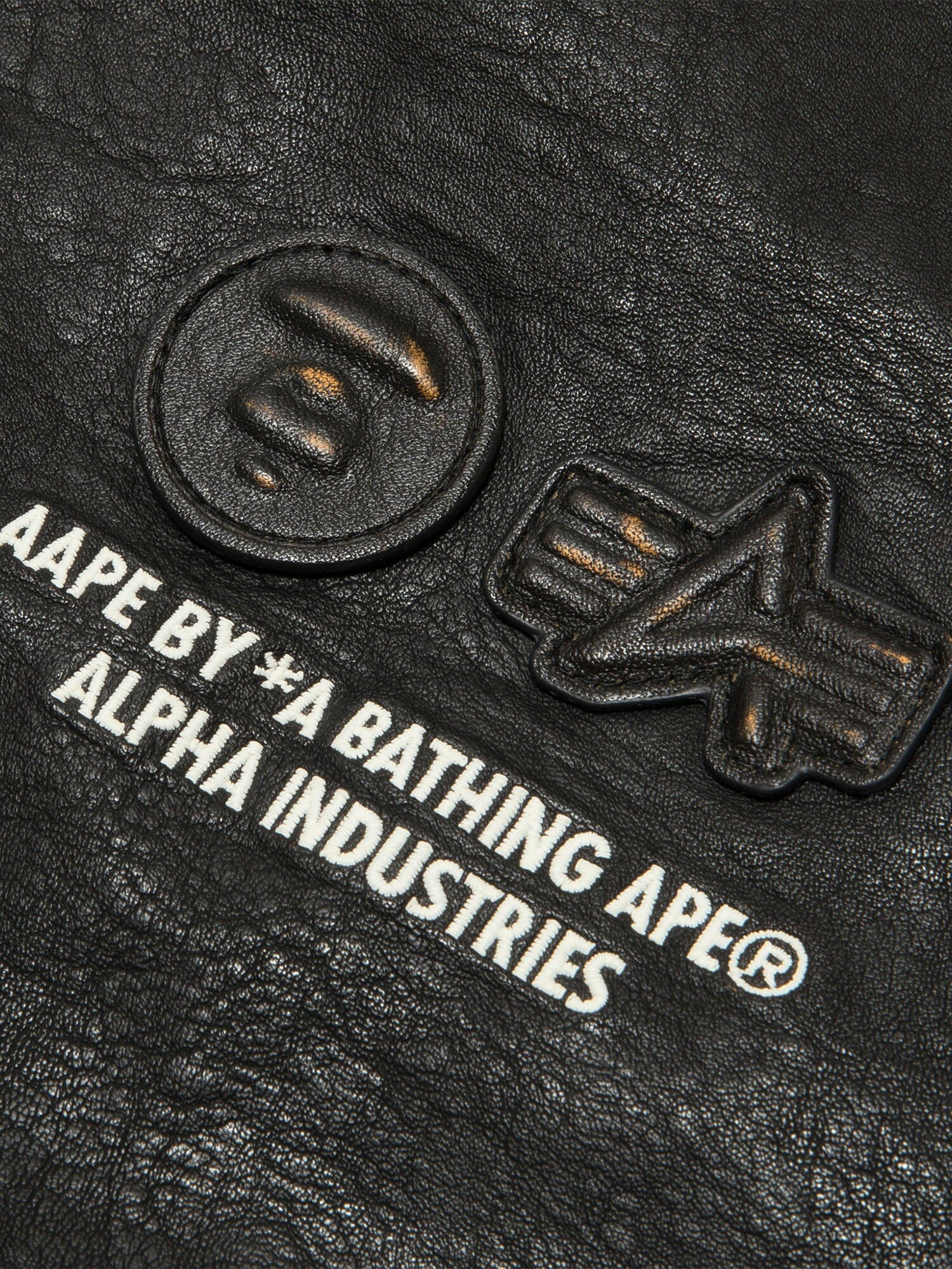 Aape X Alpha Pu Leather Quilted Jacket by Alpha Industries, black textured material with embossed logos and printed text, MA-1 design.