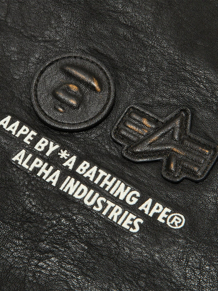 Aape X Alpha Pu Leather Quilted Jacket by Alpha Industries, black textured material with embossed logos and printed text, MA-1 design.