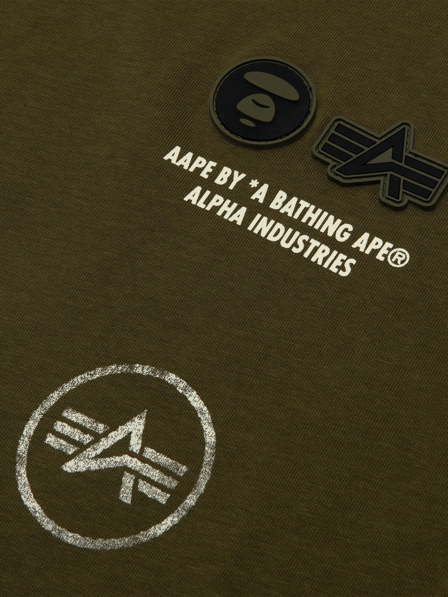 Close-up of green fabric from the Alpha Industries Tee with AAPE logo and graphic designs, featuring a vintage distressed effect.