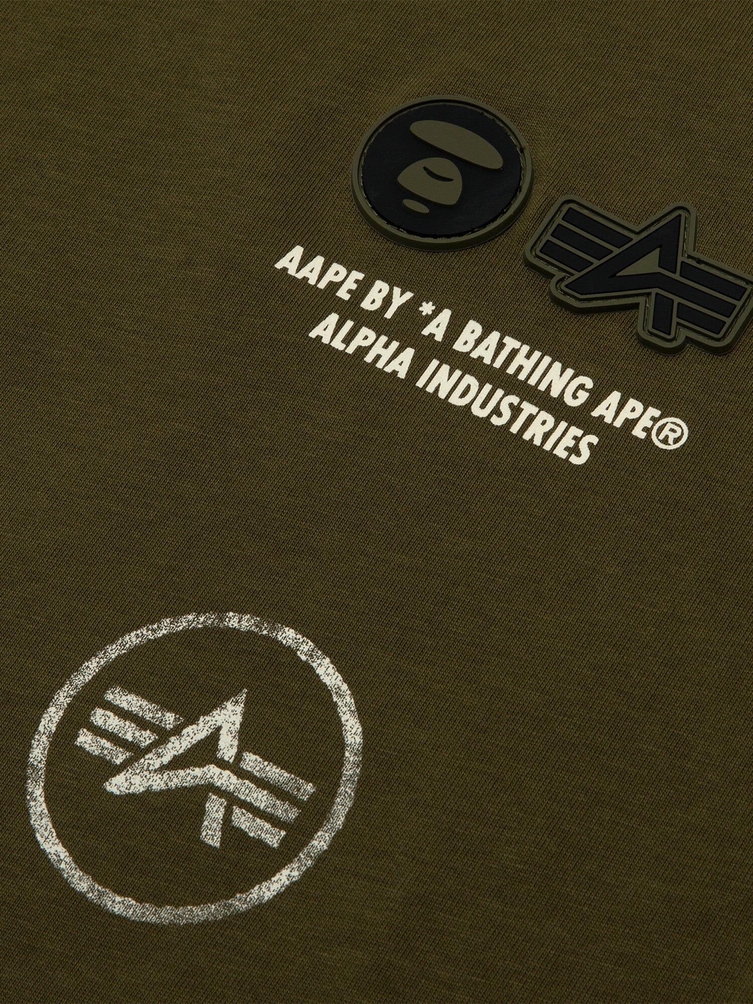 Close-up of green fabric from the Alpha Industries Tee with AAPE logo and graphic designs, featuring a vintage distressed effect.