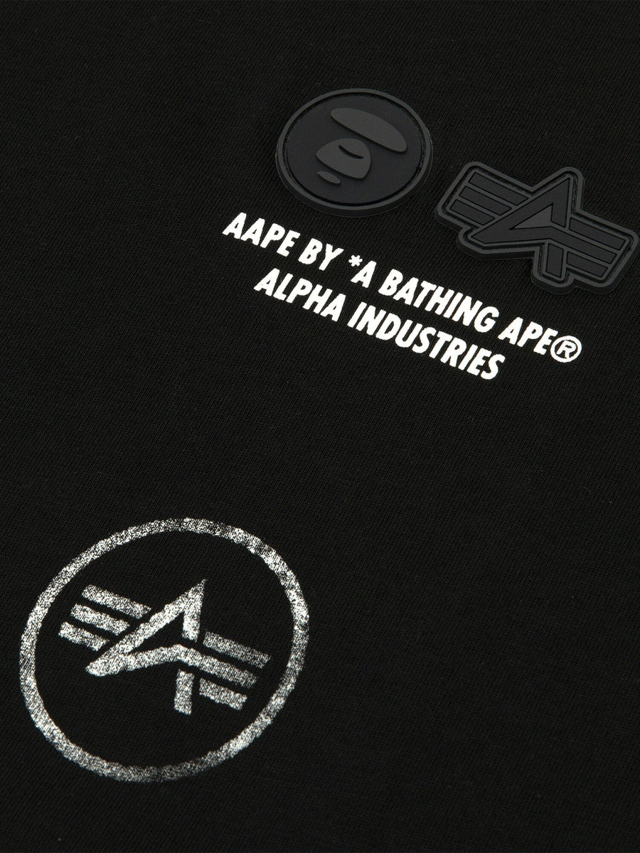 Close-up of the AAPE X Alpha Industries Somewhere In Universe Tee 
 featuring black fabric with graphic AAPE BY *A BATHING APE® ALPHA INDUSTRIES and logos.