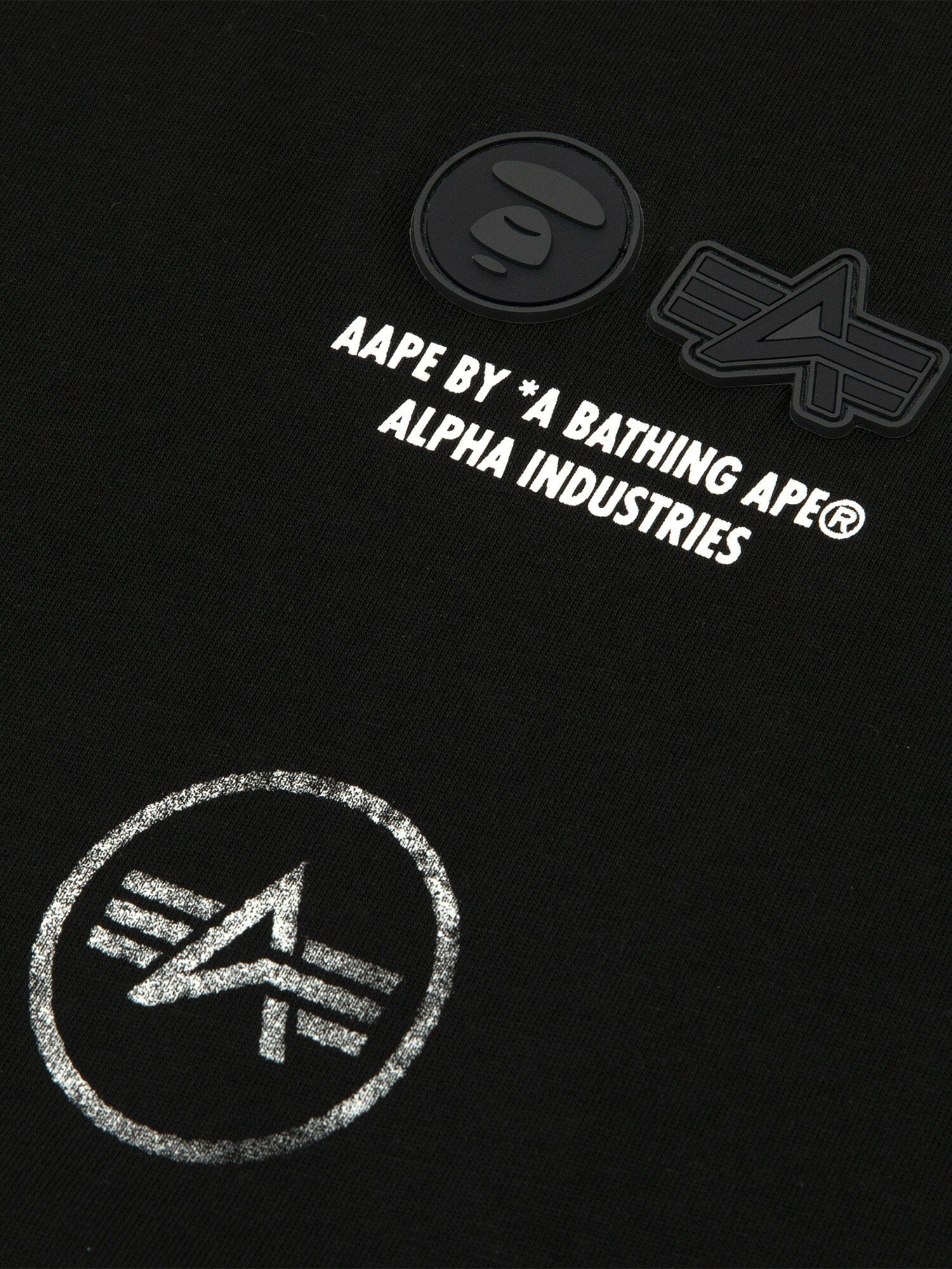 Close-up of the AAPE X Alpha Industries Somewhere In Universe Tee 
 featuring black fabric with graphic AAPE BY *A BATHING APE® ALPHA INDUSTRIES and logos.