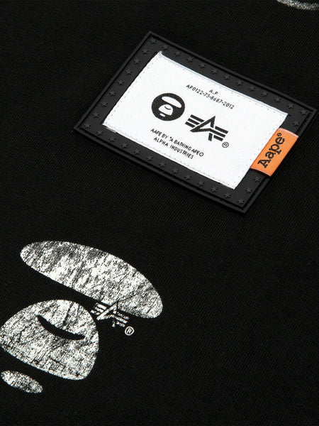 Close-up of the Black AAPE x Alpha Industries Somewhere in Universe Tee with Vintage Distressed Look, AAPE Logo Patch, White Graphics, Small Orange Tag.