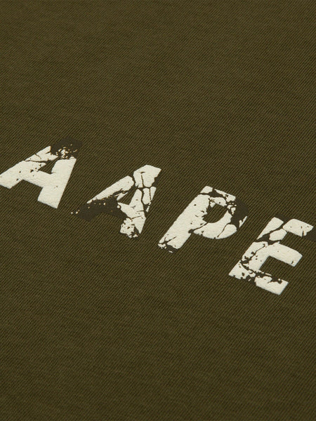 Close-up of the AAPE X Alpha Somewhere In Universe Tee by Alpha Industries. Olive green fabric with AAPE in distressed white font. 