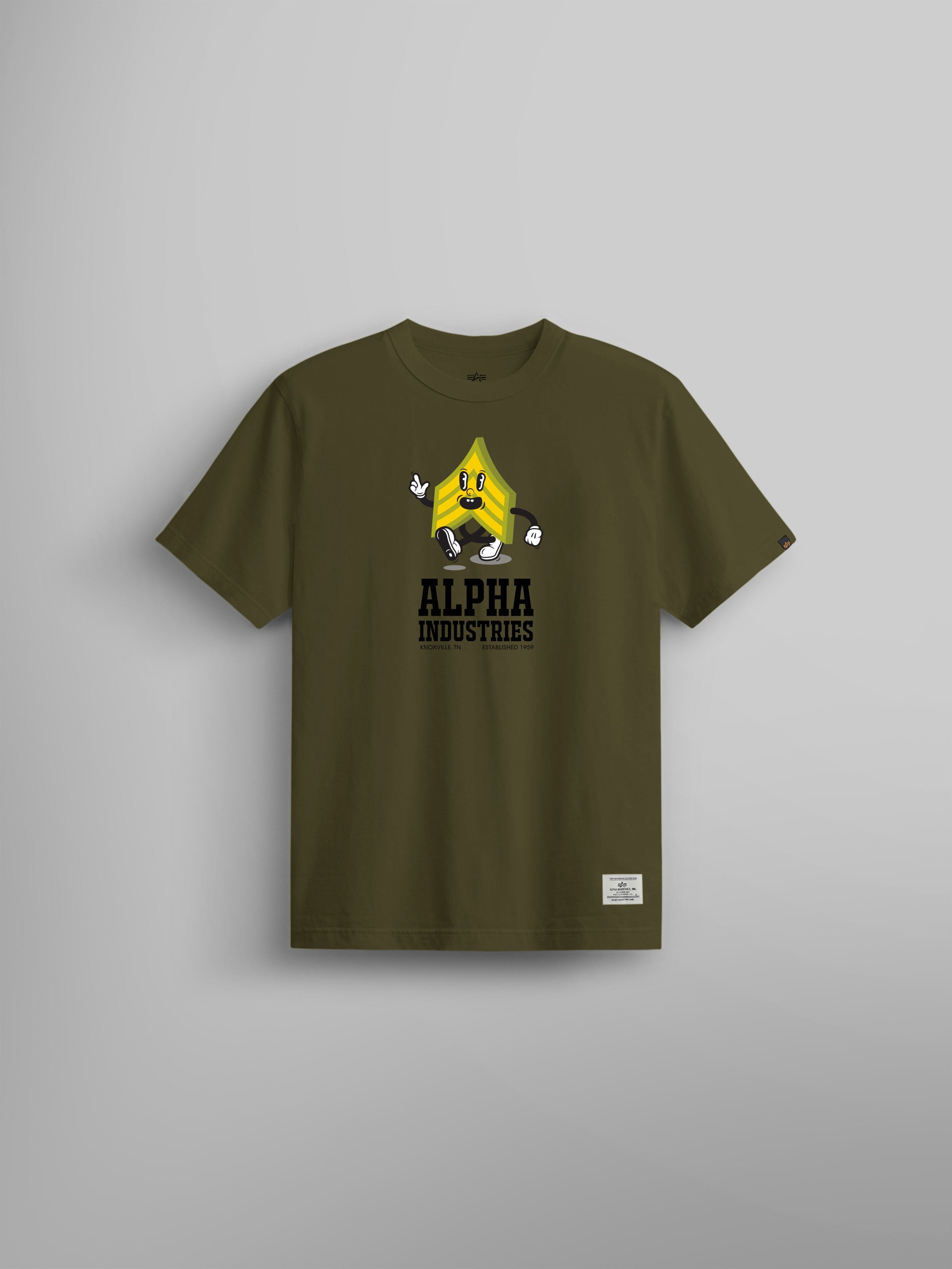 Alpha Badge Tee by Alpha Industries, olive t-shirt with cartoon yellow character, ALPHA INDUSTRIES text on front, Alpha Badge print, small white patch near bottom hem.