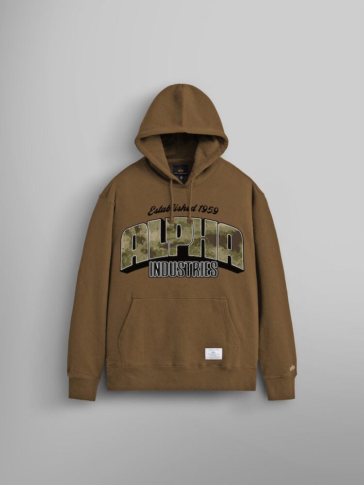 The Alpha Camo Logo Hoodie by Alpha Industries, showcases the brand name prominently on the front. Made from durable heavy cotton in a coyote brown color, it includes a front pocket and a small label at the bottom. 