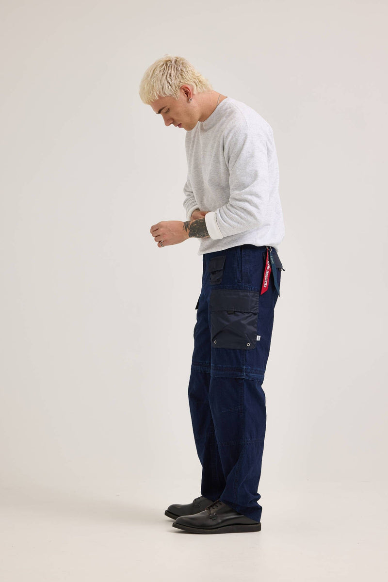 A person in a gray sweater and Alpha X Lee Convertible Cargo Pant by Alpha Industries stands, looking down at their hands.