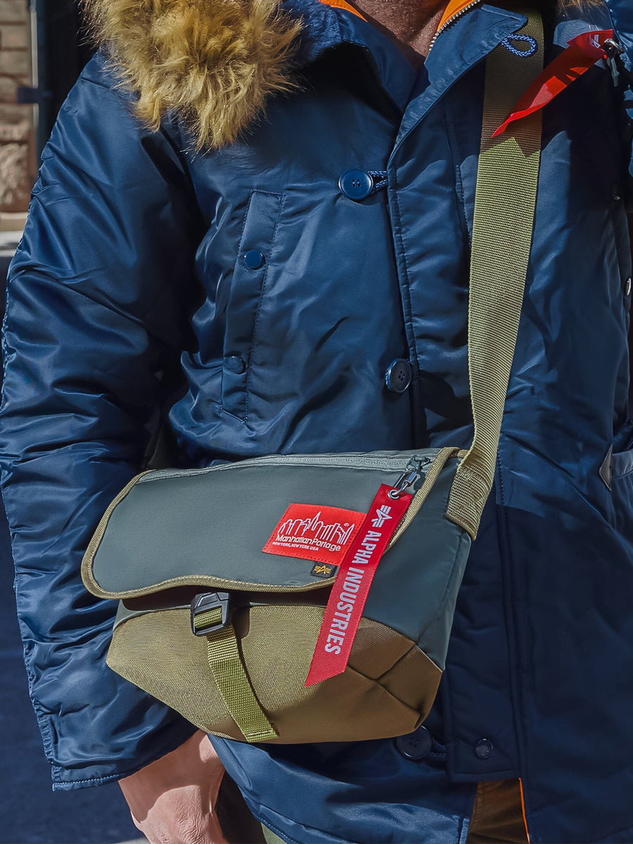 Alpha X Manhattan Portage Nylon Messenger Bag SM by Alpha Industries, blue nylon with red keychain, high-vis rescue orange accents, fur-trimmed hood.