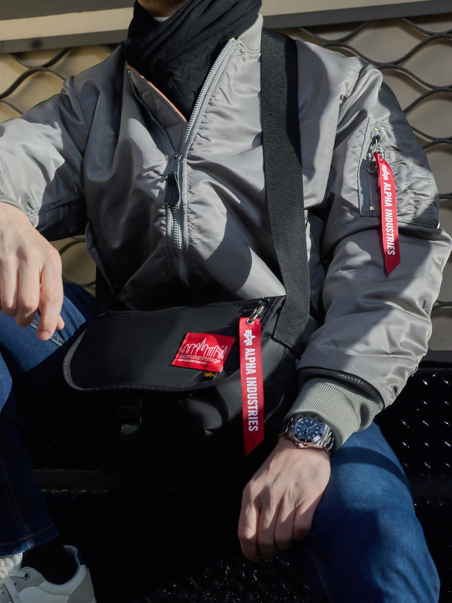 Alpha X Manhattan Portage Nylon Messenger Bag SM by Alpha Industries, gray with red Remove Before Flight tags and rescue orange high-vis details; MA-1 bomber jacket, gray.