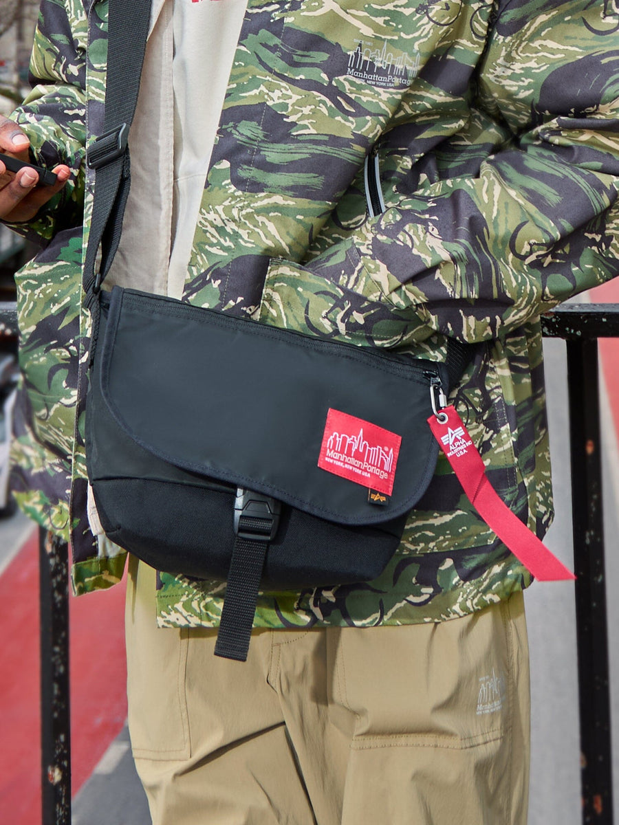 Alpha X Manhattan Portage Nylon Messenger Bag SM by Alpha Industries in green camo, flight nylon material, red logo patch, hi-vis rescue orange keychain strap.