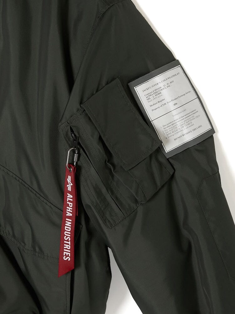 A close-up of a sleeve from the Alpha Industries x N. Hoolywood CWU-45P, showcasing a pocket, Alpha Industries tag, and a patch with text details, in dark green with a detachable hood.