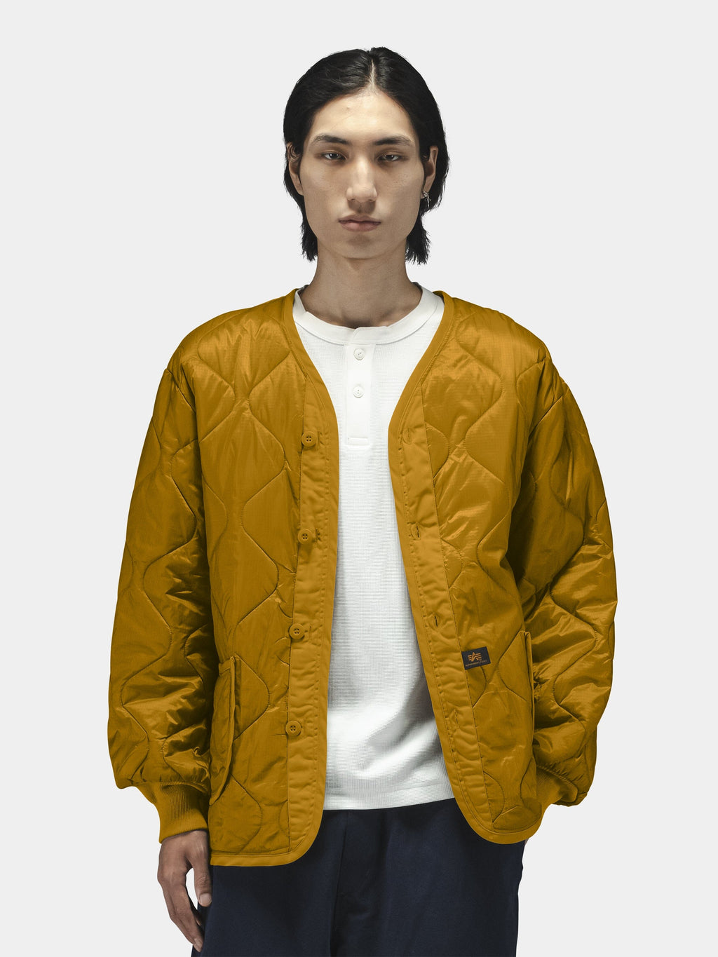 Alpha Industries Als/92 Liner in mustard yellow, worn over a white shirt and dark pants.