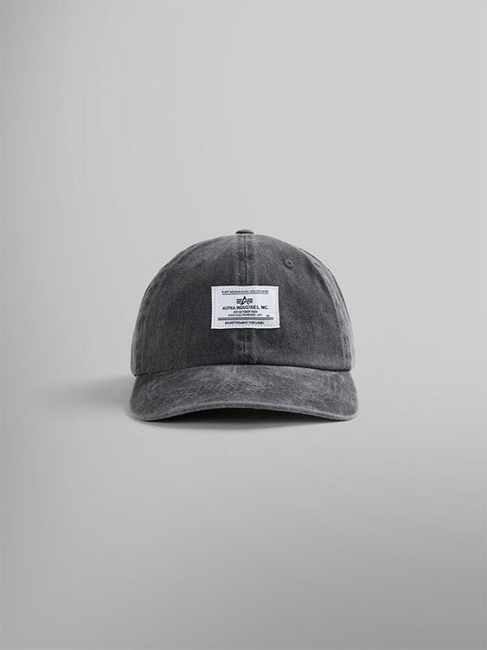 The Battlewash Cap by Alpha Industries is a black baseball cap with a vintage-inspired design. It features a white rectangular patch on the front showcasing distinctive Alpha Industries logo and text.