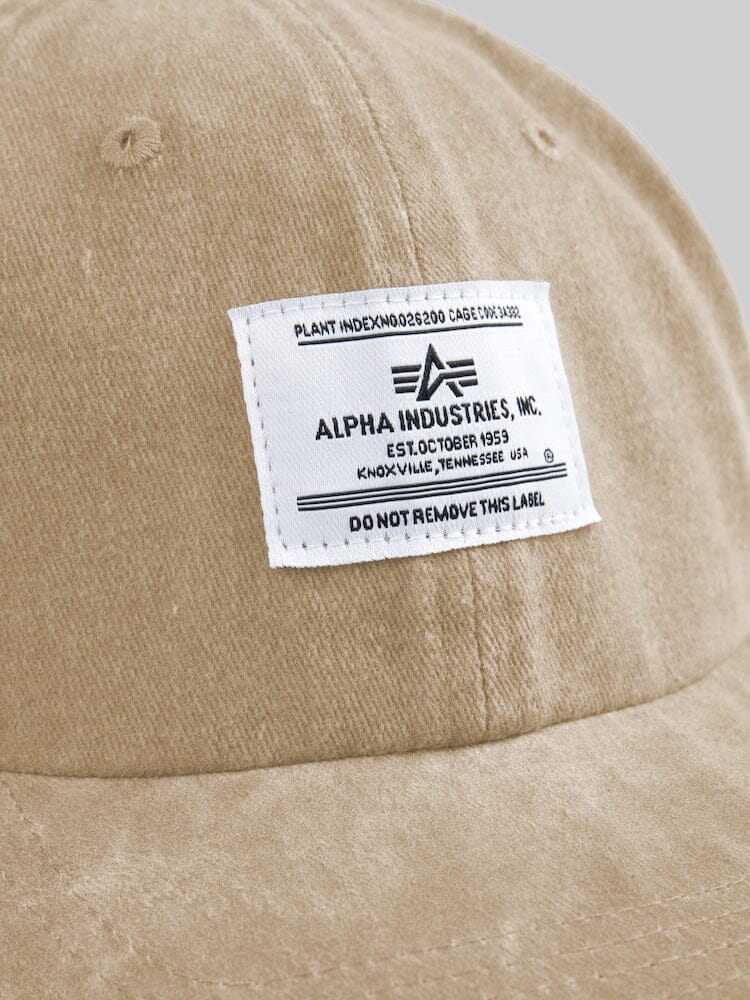 Close-up of the Battlewash Cap by Alpha Industries, a vintage-inspired khaki baseball cap showcasing a white label with Alpha Industries and manufacturing details.