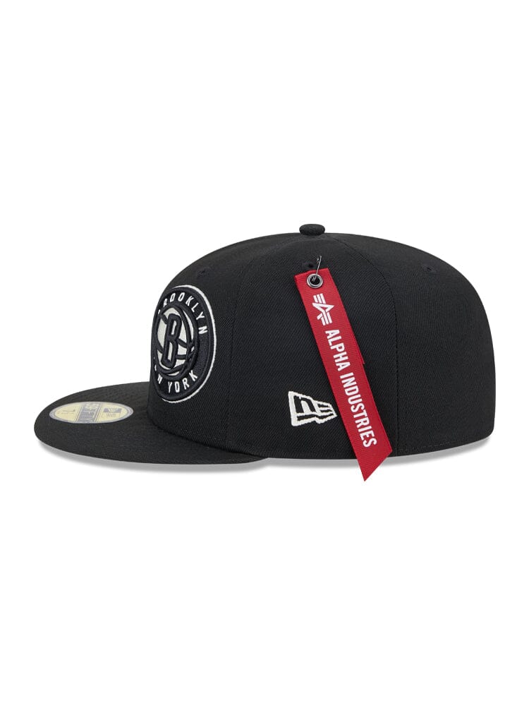 Introducing the Brooklyn Nets x Alpha x New Era 59Fifty Fitted Cap, a stylish black baseball cap with a Brooklyn team logo, flat brim, and a striking red Alpha Industries tag.