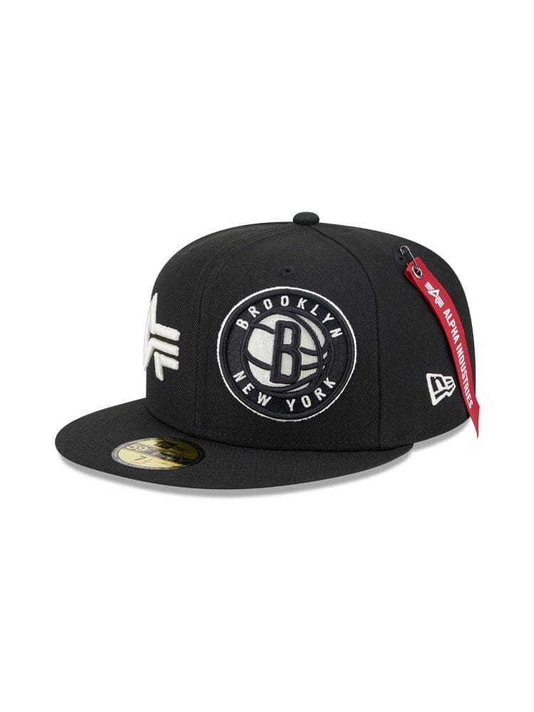 A Black Brooklyn Nets x Alpha Industries x New Era 59Fifty Fitted Cap, featuring a flat brim with the team logo and city name on the front, complete with a red tag attached to the brim.