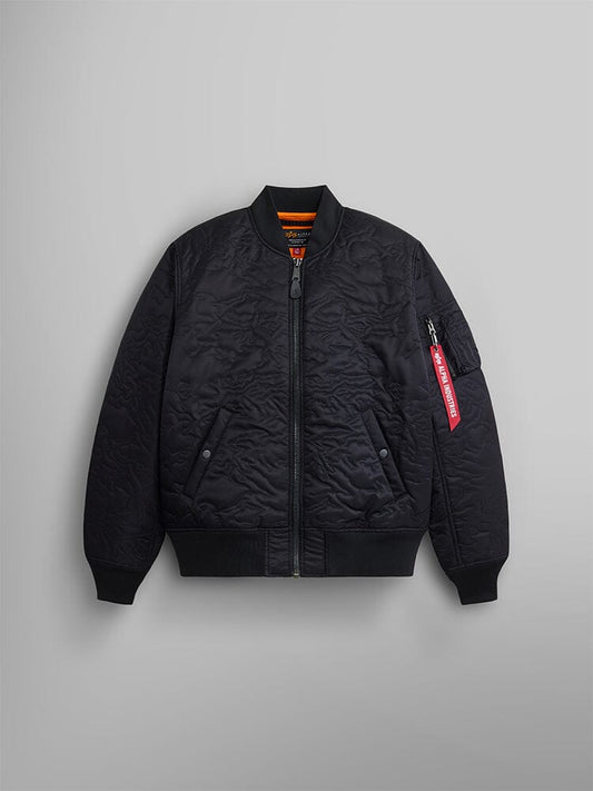 The Camo Quilted MA-1 Bomber Jacket by Alpha Industries, featured in black, showcases a quilted design with an MA-1 utility pocket and distinctive red tag on the sleeve. It has a zip front and two snap-button pockets.