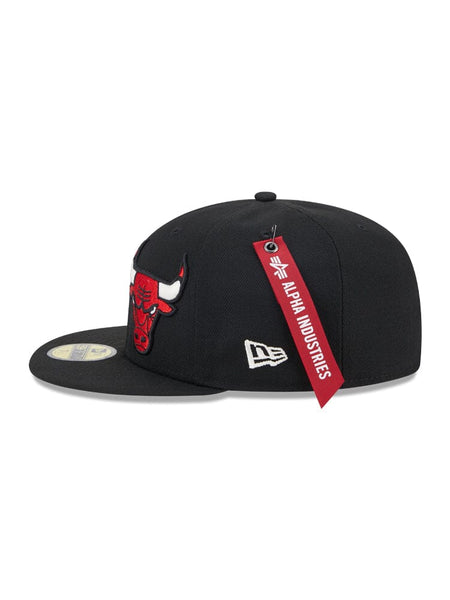 The Chicago Bulls X Alpha X New Era 59Fifty Fitted Cap, by Alpha Industries / NE-NBA, boasts a striking red bull embroidered team logo on the front, a sleek white logo on the side, and a vivid red Alpha Industries® tag attached.
