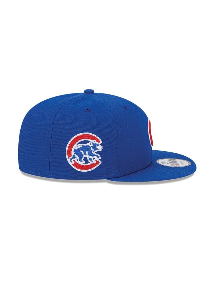 The Chicago Cubs x Alpha x New Era 950 Cap by Alpha Industries features a blue design with a red and white Chicago Cubs team logo, showcasing a bear inside a "C" on the side. It comes with a snapback closure for an adjustable fit, and its model number is FW24-NE-MLB.