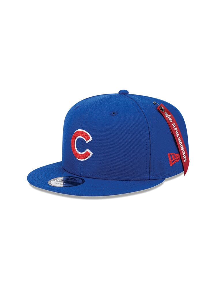 Chicago Cubs x Alpha x New Era 950 Cap by Alpha Industries features a bold red C team logo on the front, a side tag labeled with Alpha Industries, and an easily adjustable snapback closure. The cap is in a vibrant blue color.