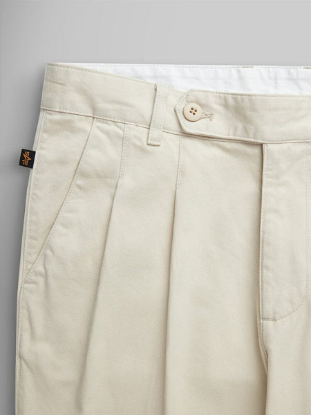 Alpha Industries Classic Trouser in beige cotton with pleats, button closure, belt loops, and black-and-yellow tag on waistband.