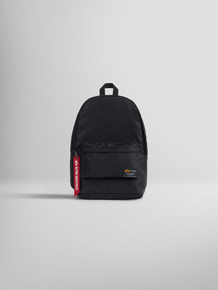The Crew Backpack by Alpha Industries is an elegant black flight nylon backpack with a front pocket and a distinctive red Remove Before Flight tag.