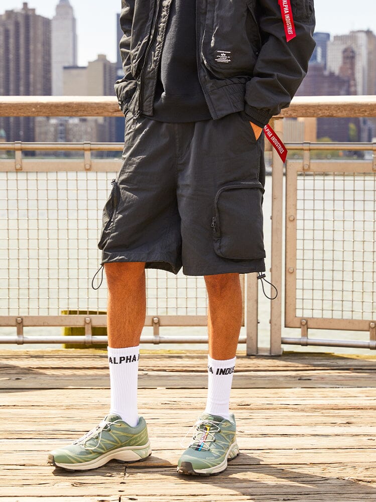 Alpha Industries Cwu 36/P Pull On Short, Black Jacket, White Socks With Alpha Industries Text, Light Green Sneakers.