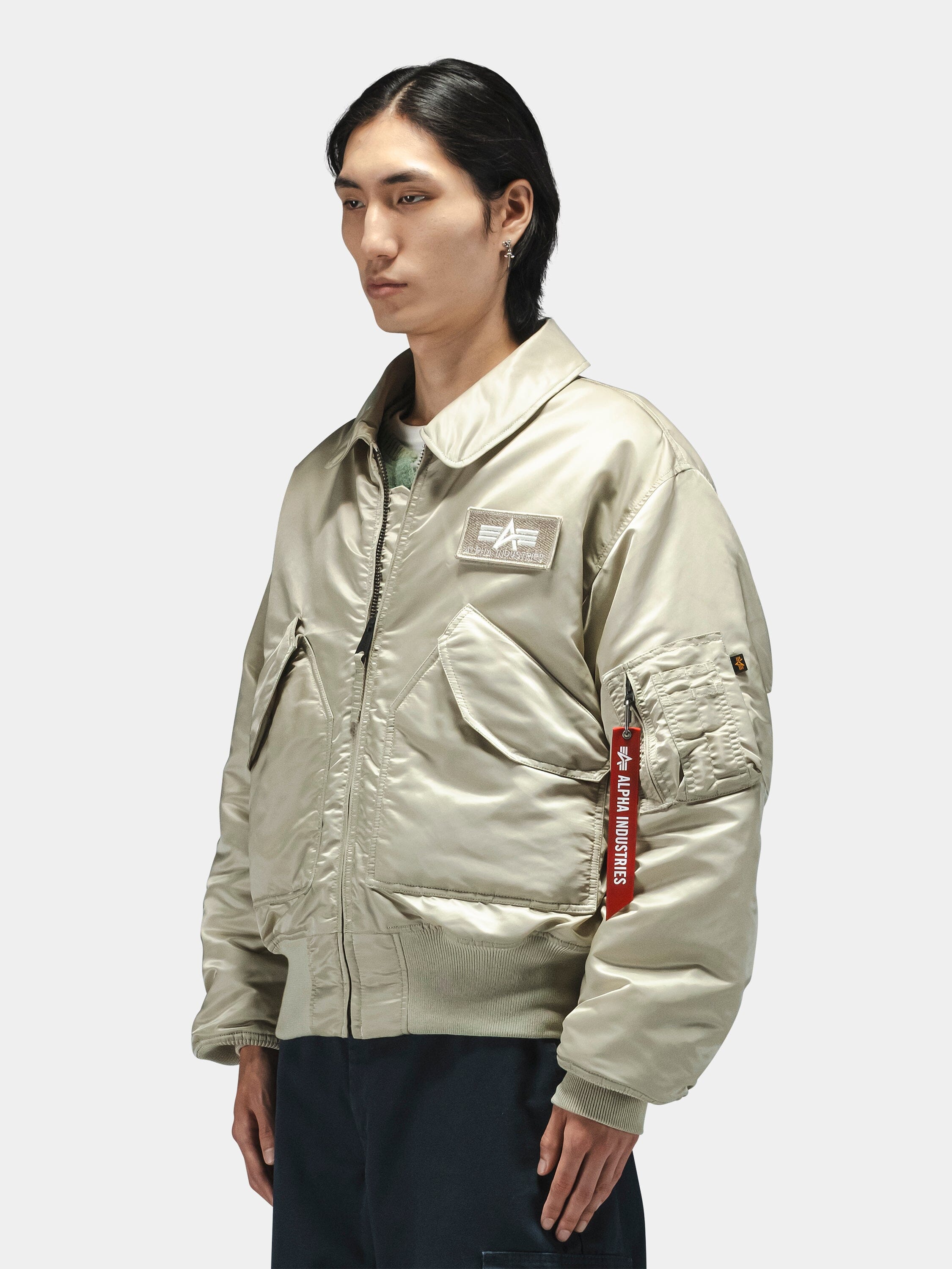 Alpha Industries Cwu 45/P Bomber Jacket in light beige with chest patch and red Remove Before Flight tag on the sleeve.