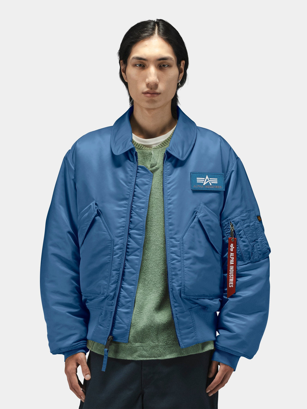 Alpha Industries Cwu 45/P Bomber Jacket in blue with chest patch, layered over green sweater.