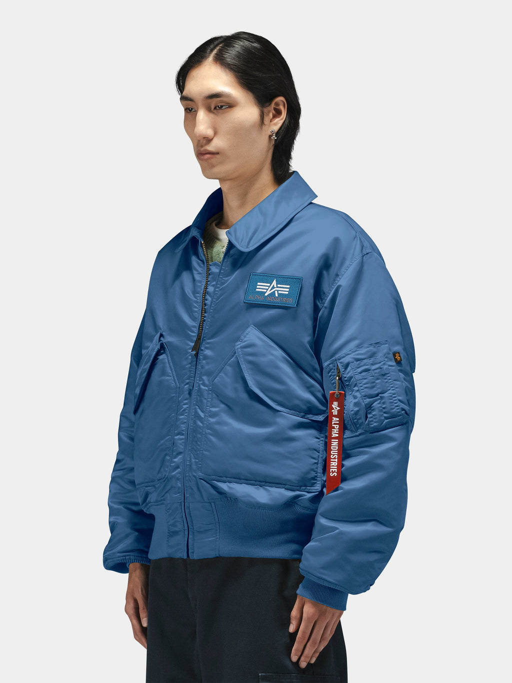Alpha Industries Cwu 45/P Bomber Jacket in blue with flight insignia patch on chest and red "Remove Before Flight" tag on sleeve.